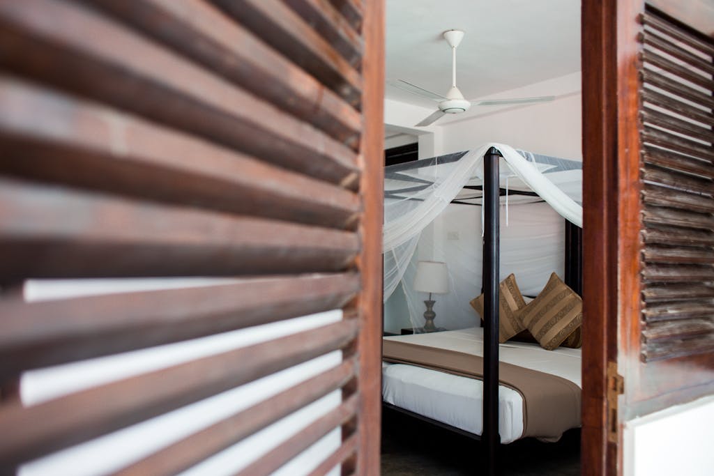 Elegant bedroom with four-poster bed seen through wooden shutters, exuding a serene ambiance.